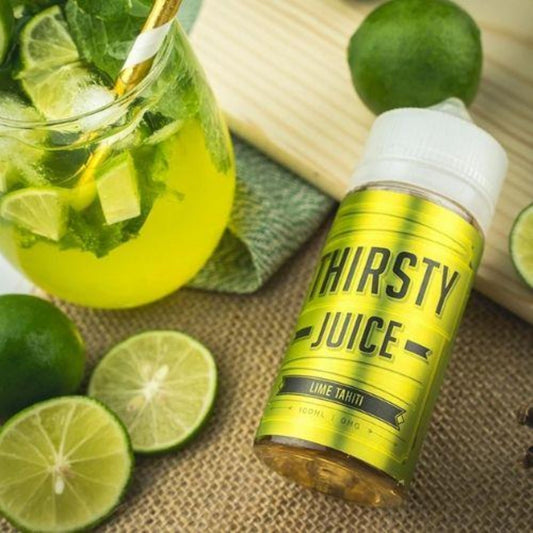 Thirsty Juice Co | Lime Tahiti | 100ml bottle laying on the table with a whole lime and sliced lime with a glass of green lime juice