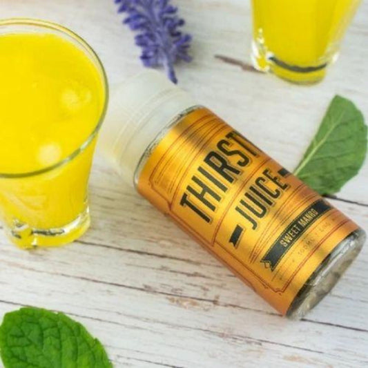 Thirsty Juice Co | Sweet Mango | 100ml bottle laying on the table with 2 glasses of mango juice and some mint leaves